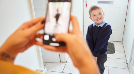 Young boy in school uniform stands in front of door for photograph, taken by out of focus mobile phone
