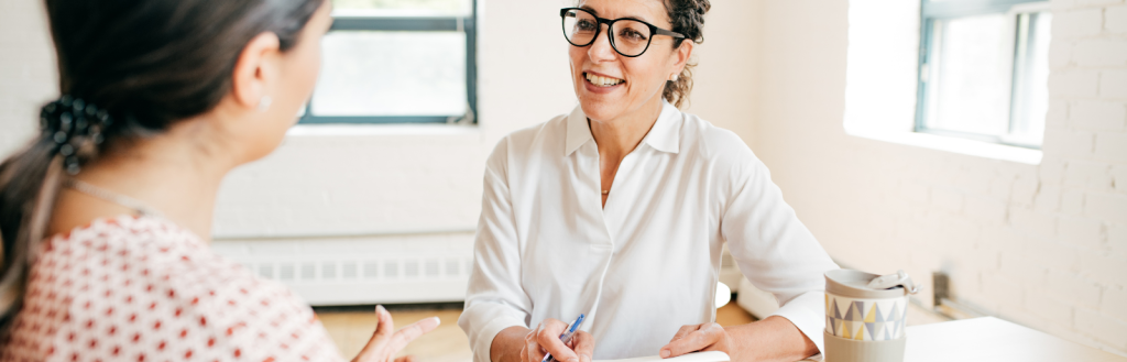 Two people talking at desk.